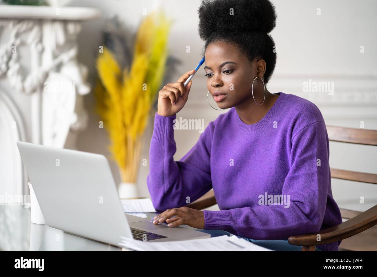 Donna studentesca afro-americana millennial con afro hairstyle navigando informazioni su laptop, preparandosi per l'esame online, guardando video corso, tenendo un Foto Stock