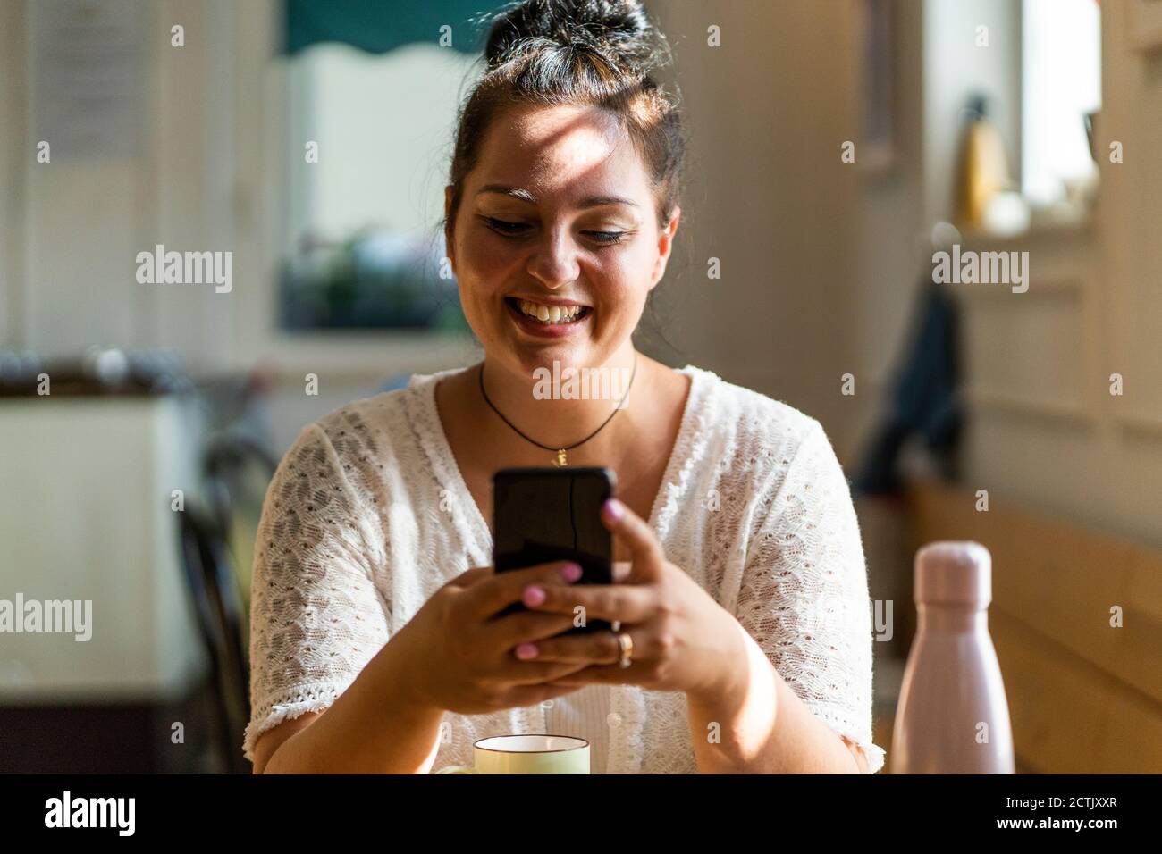 Primo piano di una donna sorridente e voluttuosa che usa il telefono cellulare mentre si è seduti nel ristorante Foto Stock