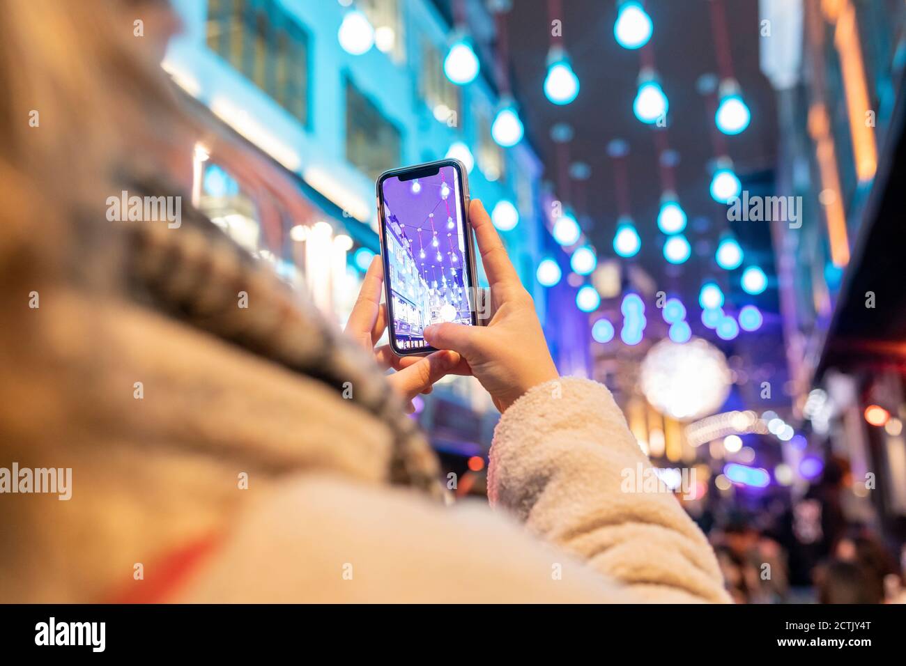 Primo piano di una donna che fotografa luci di Natale illuminate in città a. notte Foto Stock