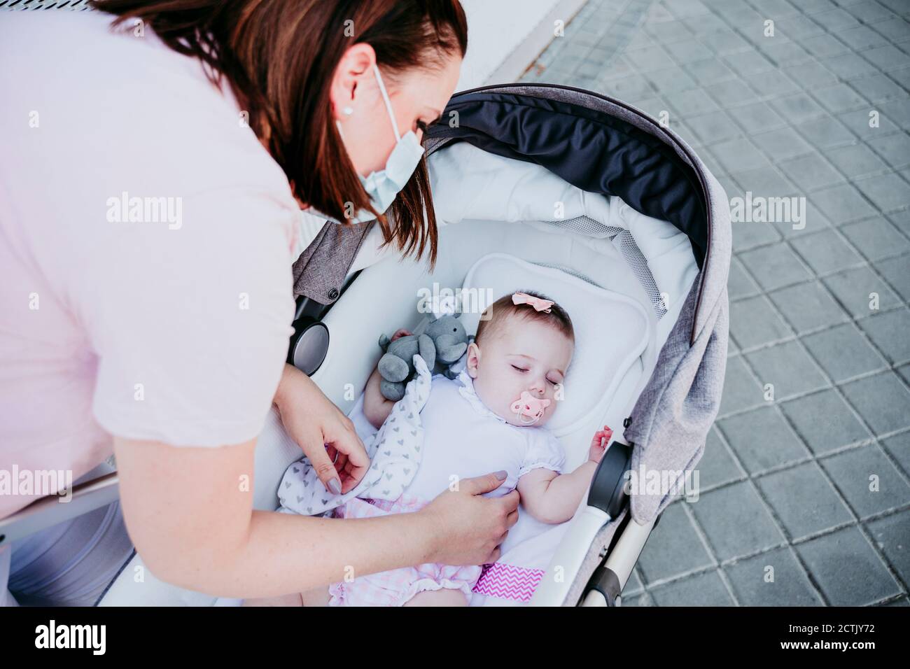 Mamma che indossa una maschera protettiva, bambina addormentata in passeggino Foto Stock