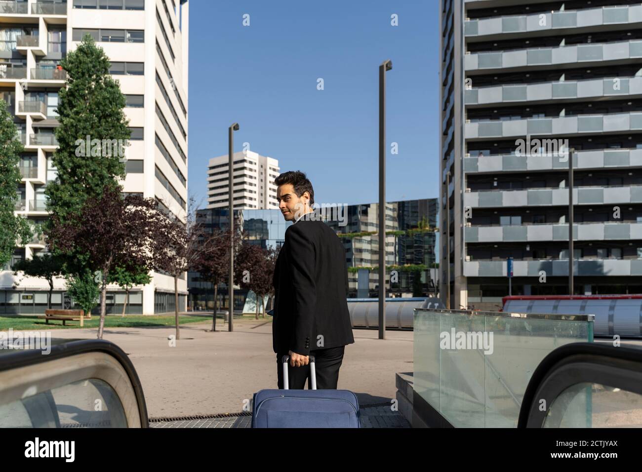 Uomo d'affari con valigia camminare sul sentiero contro cielo chiaro in città Foto Stock