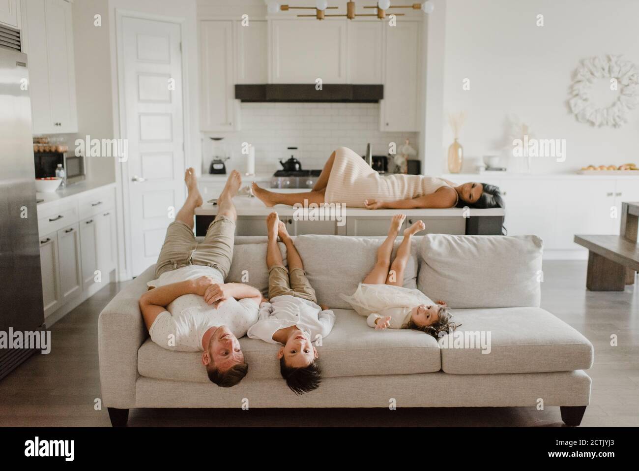 Padre sdraiato con i bambini sul divano mentre la madre si rilassa isola cucina a casa Foto Stock