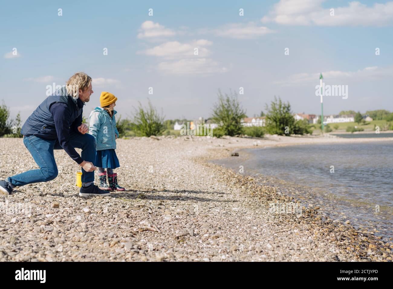 Padre e figlia che guardano il fiume mentre gettano ciottoli dentro acqua vicino riva del fiume Foto Stock