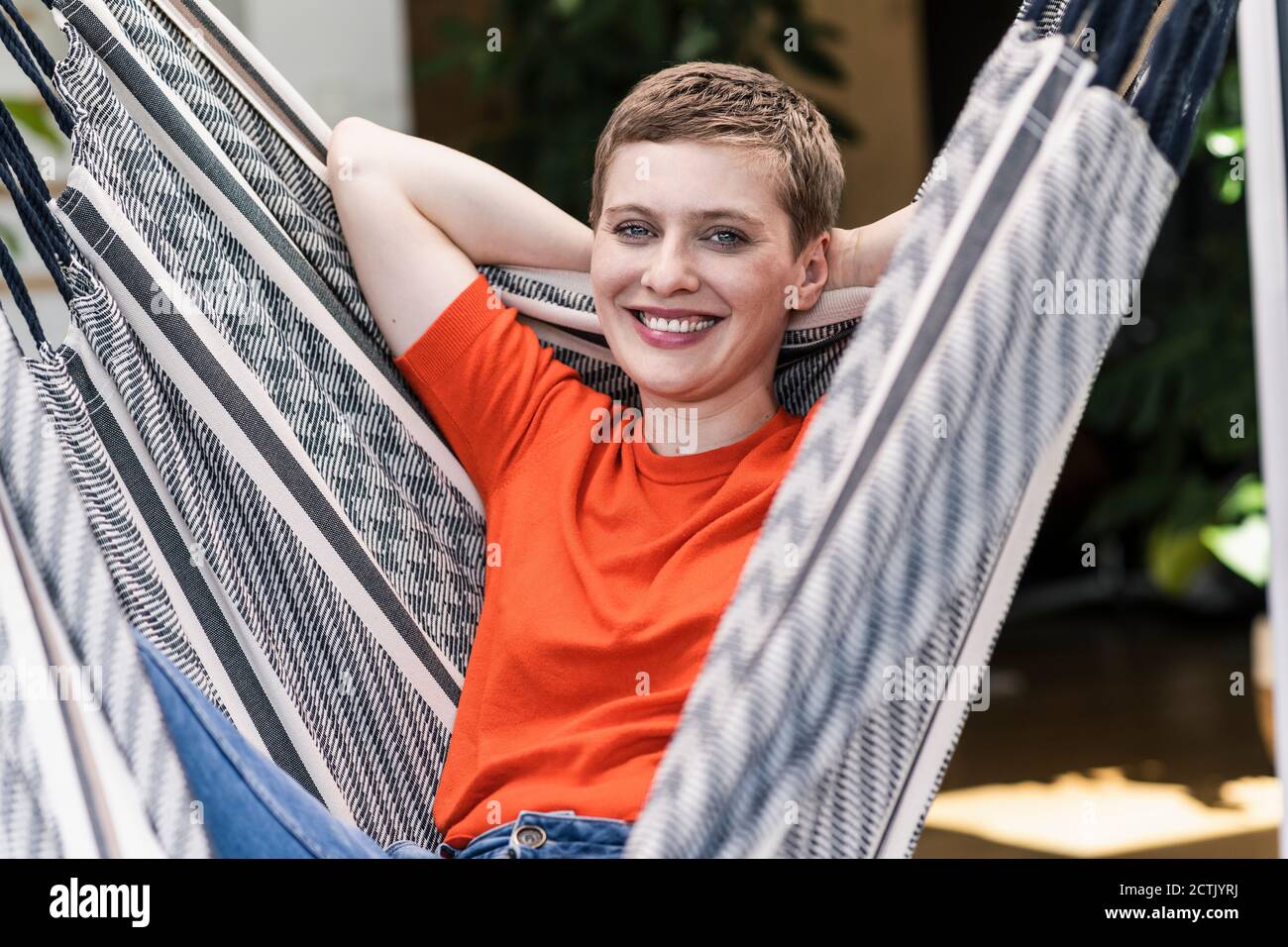 Primo piano di una bella donna sorridente con le mani dietro la testa oscillanti in portico Foto Stock