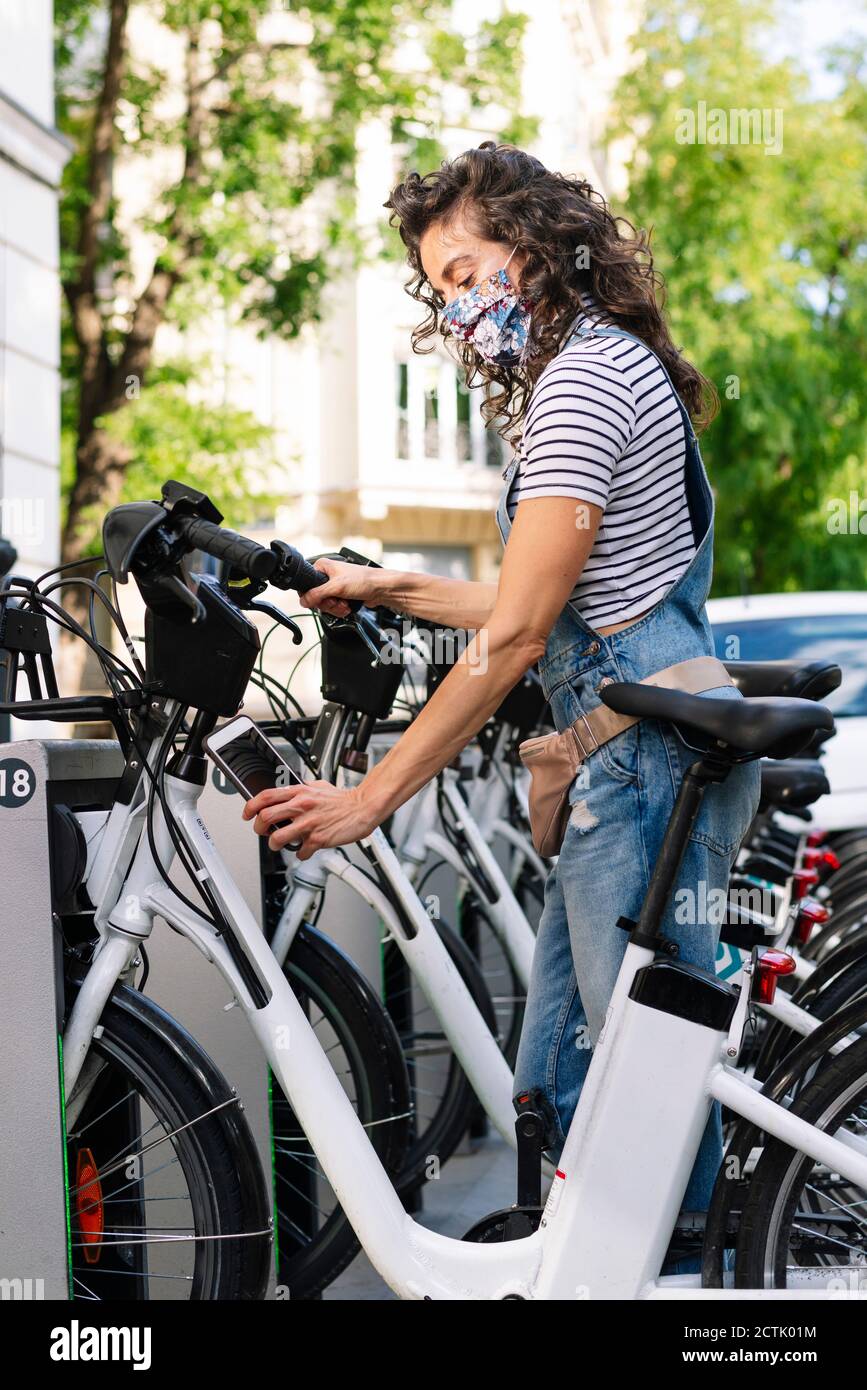 Donna che scannerizza il codice QR su bicicletta elettrica con smartphone in città Foto Stock