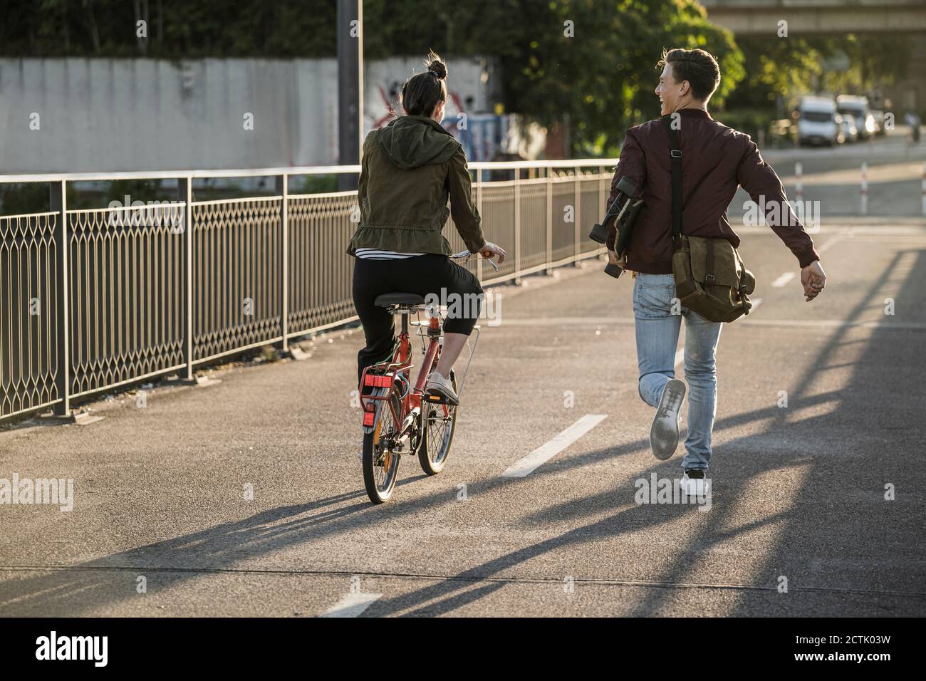 Giovane uomo che trasporta skateboard mentre corre in bicicletta da ragazza in città Foto Stock