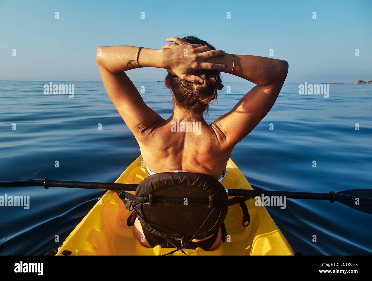 Donna con le mani dietro la testa seduta in barca contro chiaro cielo blu Foto Stock