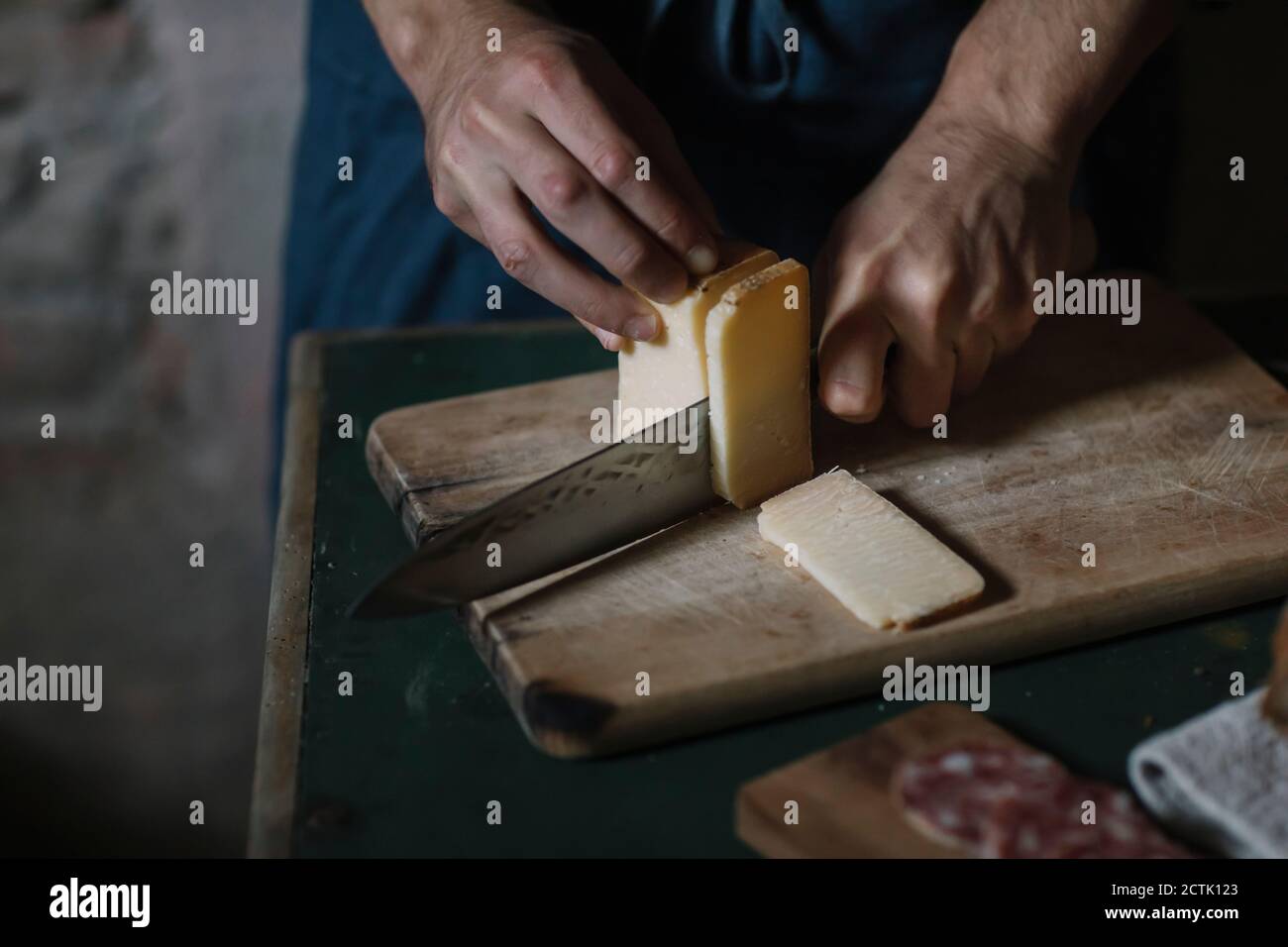 Mani di uomo che tagliano fette di formaggio artigianale a bordo a. tabella Foto Stock