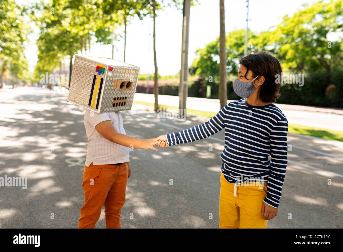 Maschera di ragazzo in faccia che dà la stretta di mano ad un amico che indossa il robot costume mentre si è in piedi su strada Foto Stock