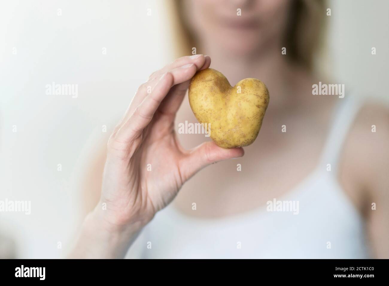 Mano della donna che tiene la patata a forma di cuore Foto Stock
