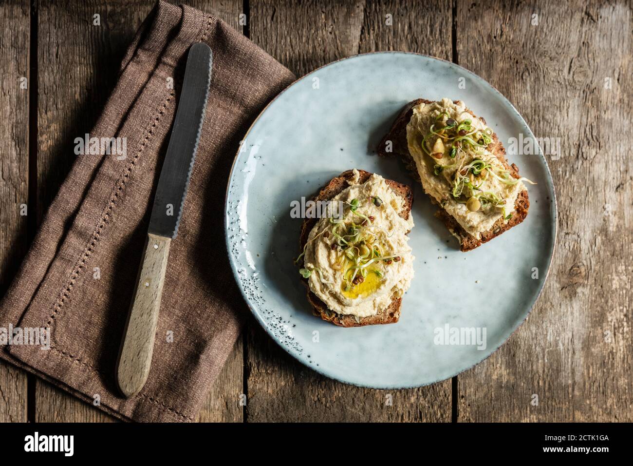 Coltello da tavola e fette di pane con hummus e germogli Foto Stock