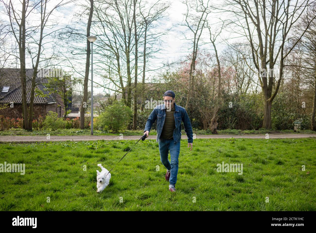 Uomo sorridente che corre con il cane su erba in cortile Foto Stock