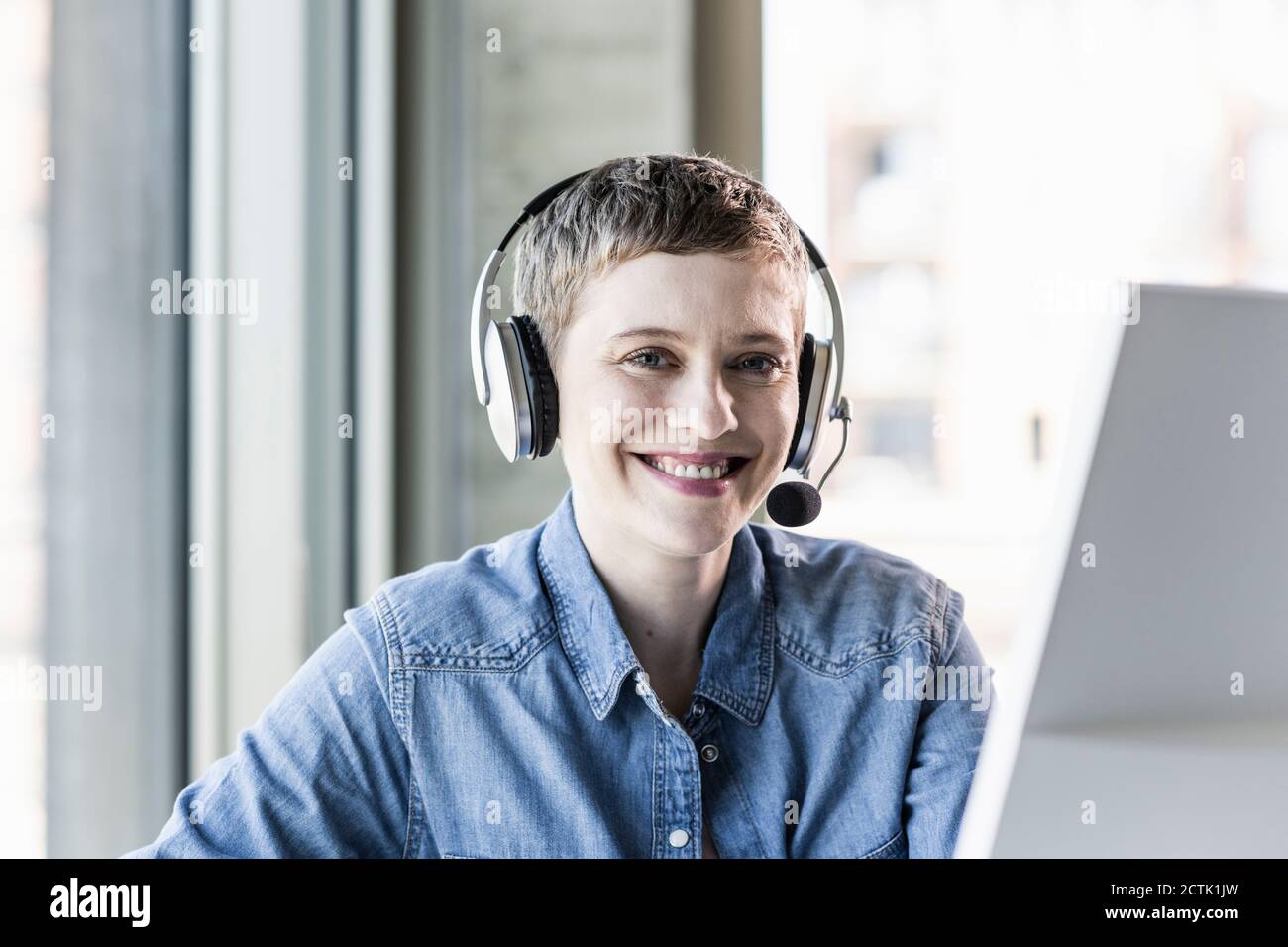 Ritratto di sorridere imprenditrice che indossa la cuffia alla scrivania in ufficio Foto Stock