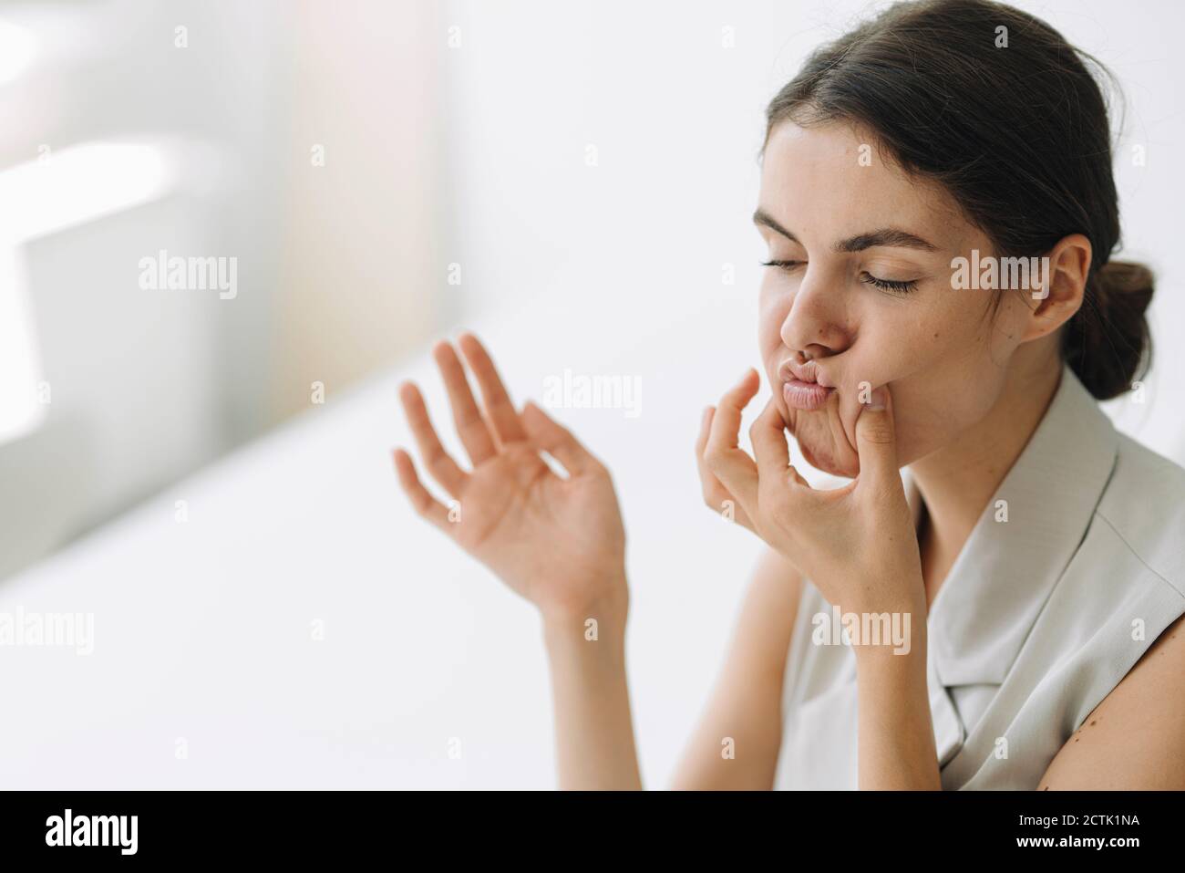 Donna divertente che fa i volti mentre si siede in ufficio Foto Stock