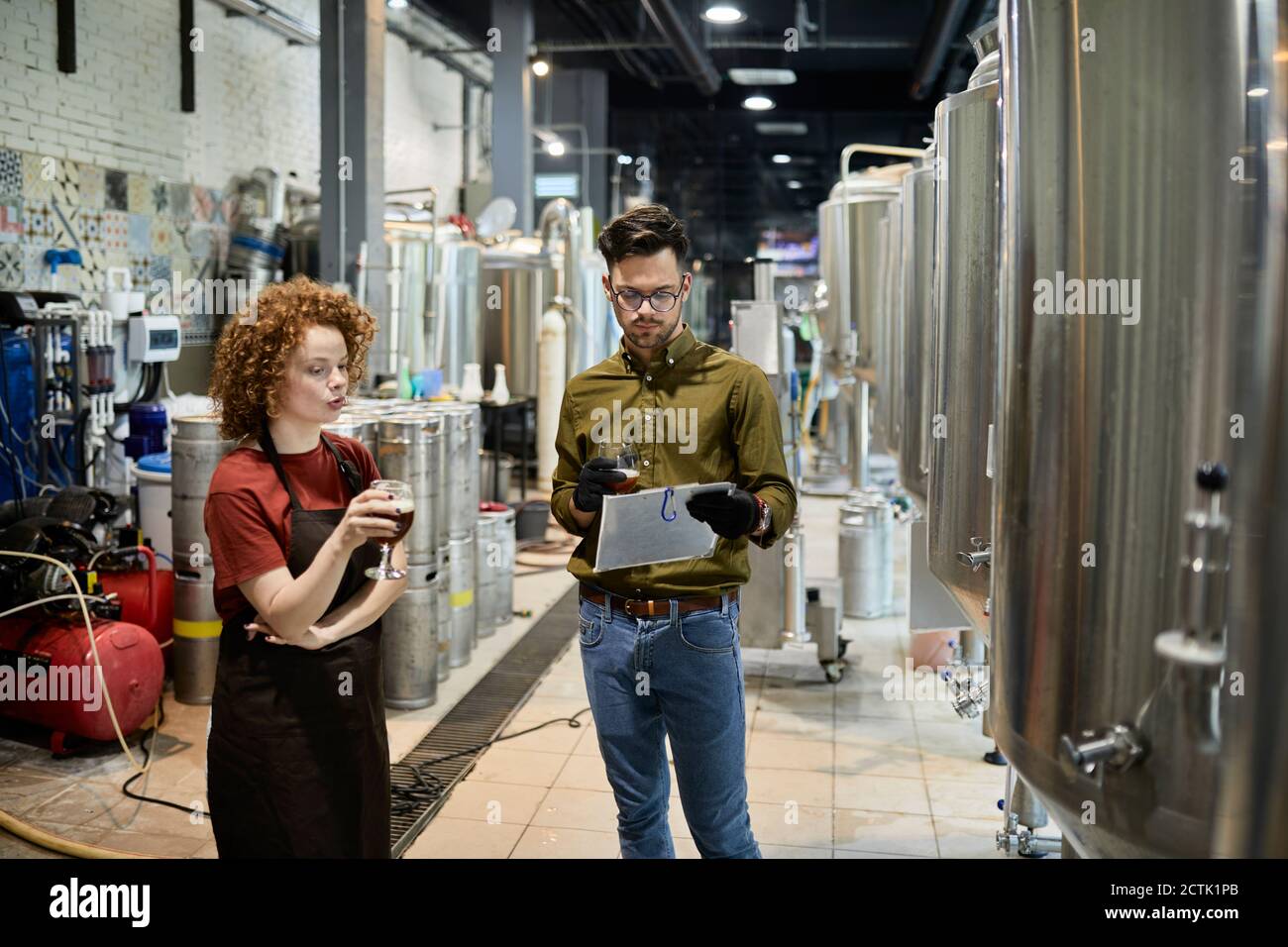 Uomo e donna che lavorano in fabbrica di birra artigianale discutere la qualità di una birra Foto Stock