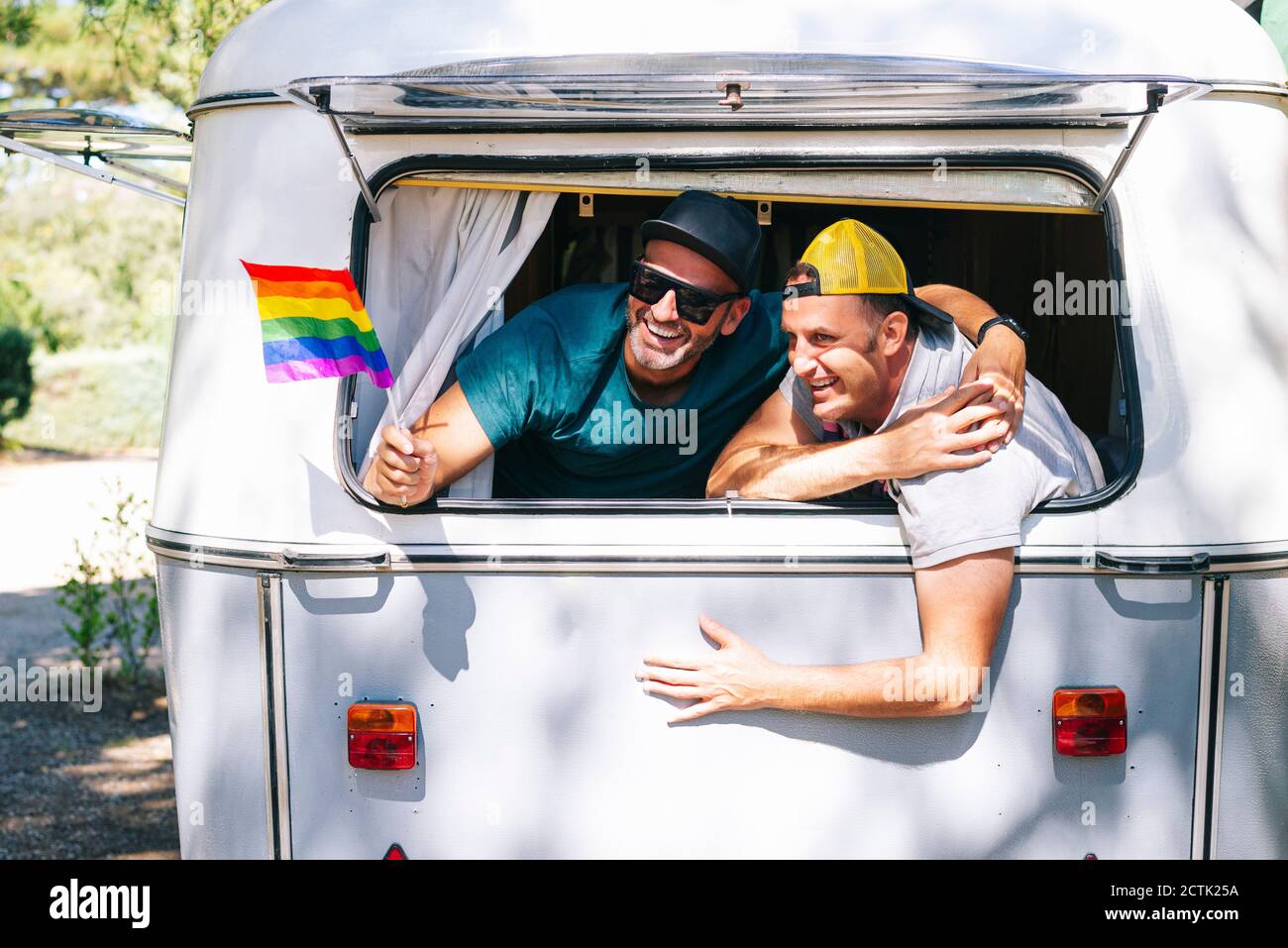 Uomini gay con bandiera arcobaleno godendosi in casa a motore Foto Stock