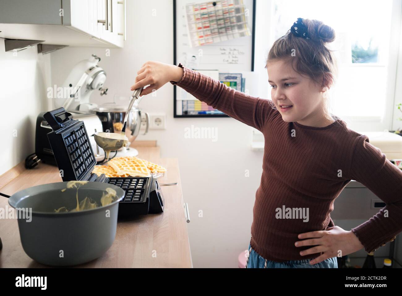 Carina ragazza con mestolo preparare waffle in cucina Foto Stock