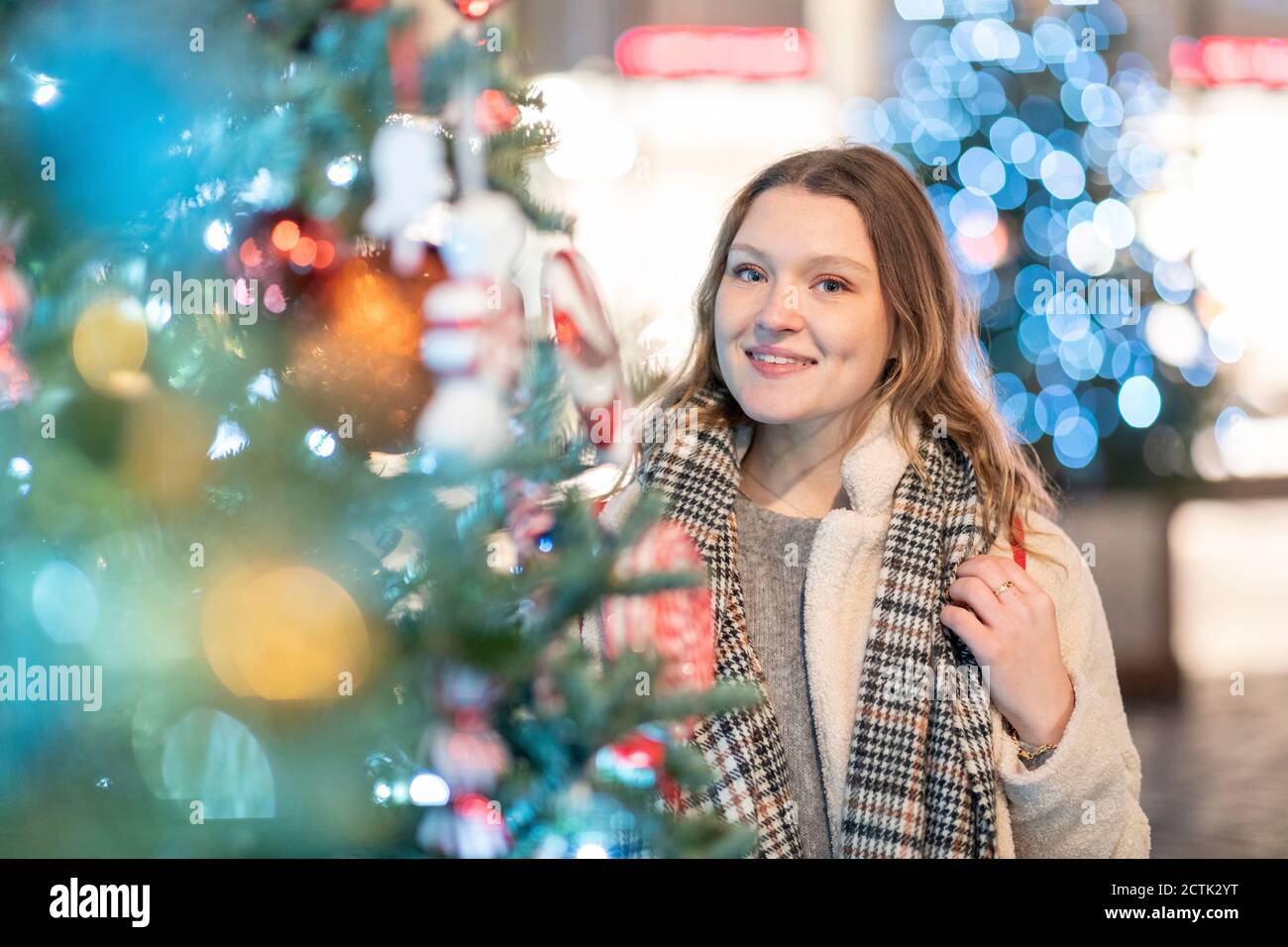 Sorridente bella donna in piedi da illuminato albero di Natale in città di notte Foto Stock