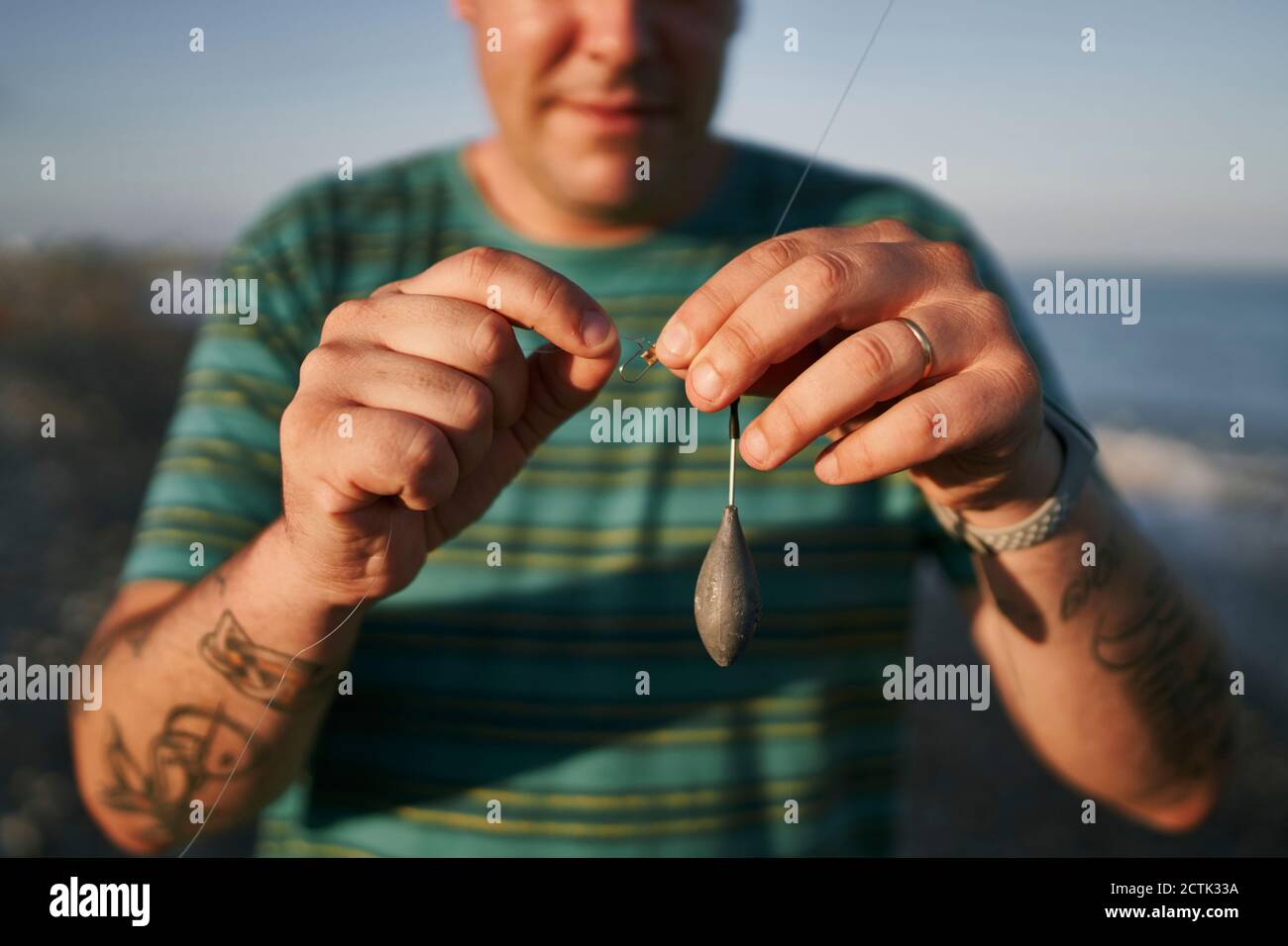 Primo piano di un uomo medio adulto che prepara la strada di pesca in spiaggia durante il tramonto Foto Stock
