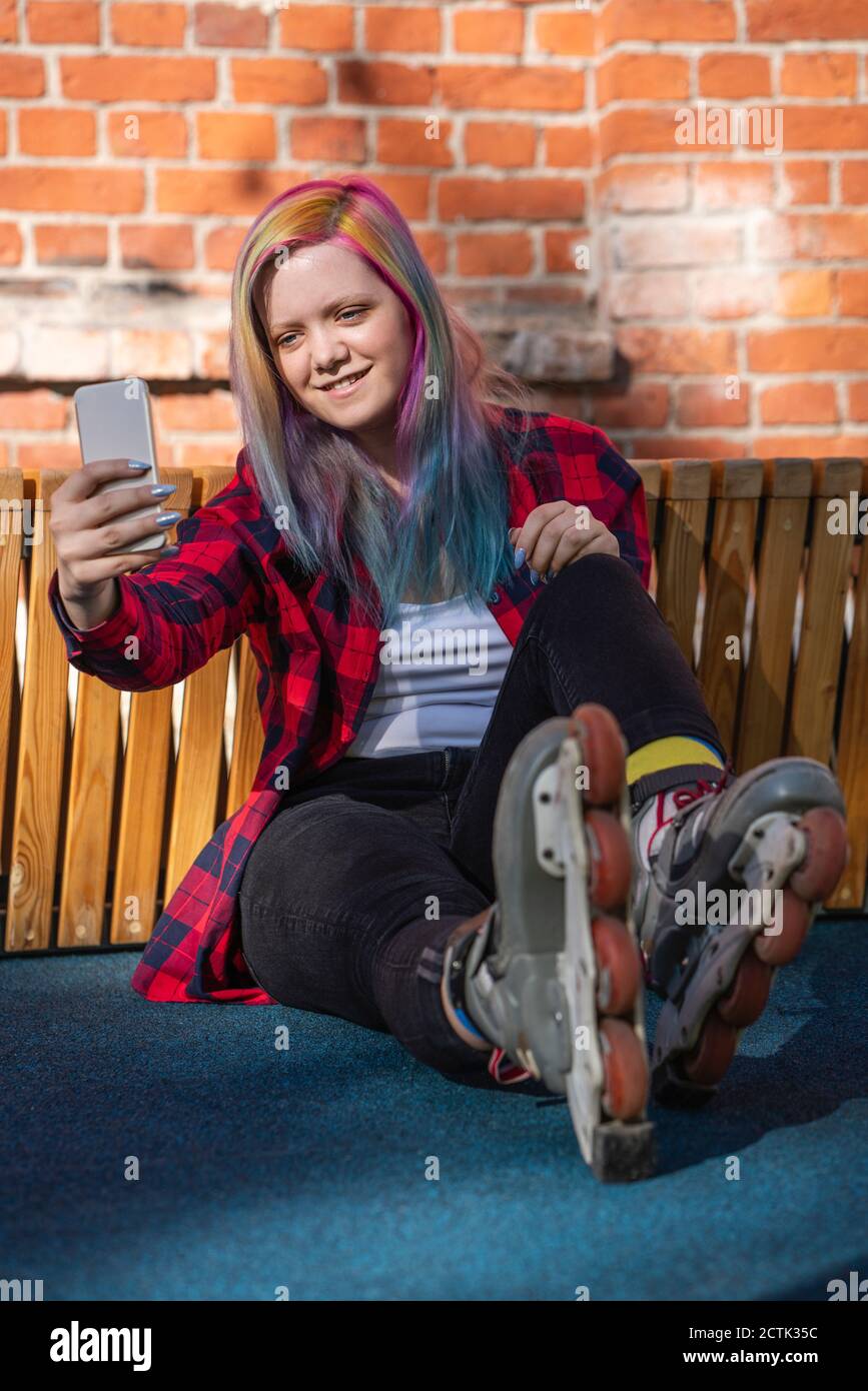 Giovane donna con capelli tinti e pattini a rotelle che prendono un selfie con il suo smartphone Foto Stock