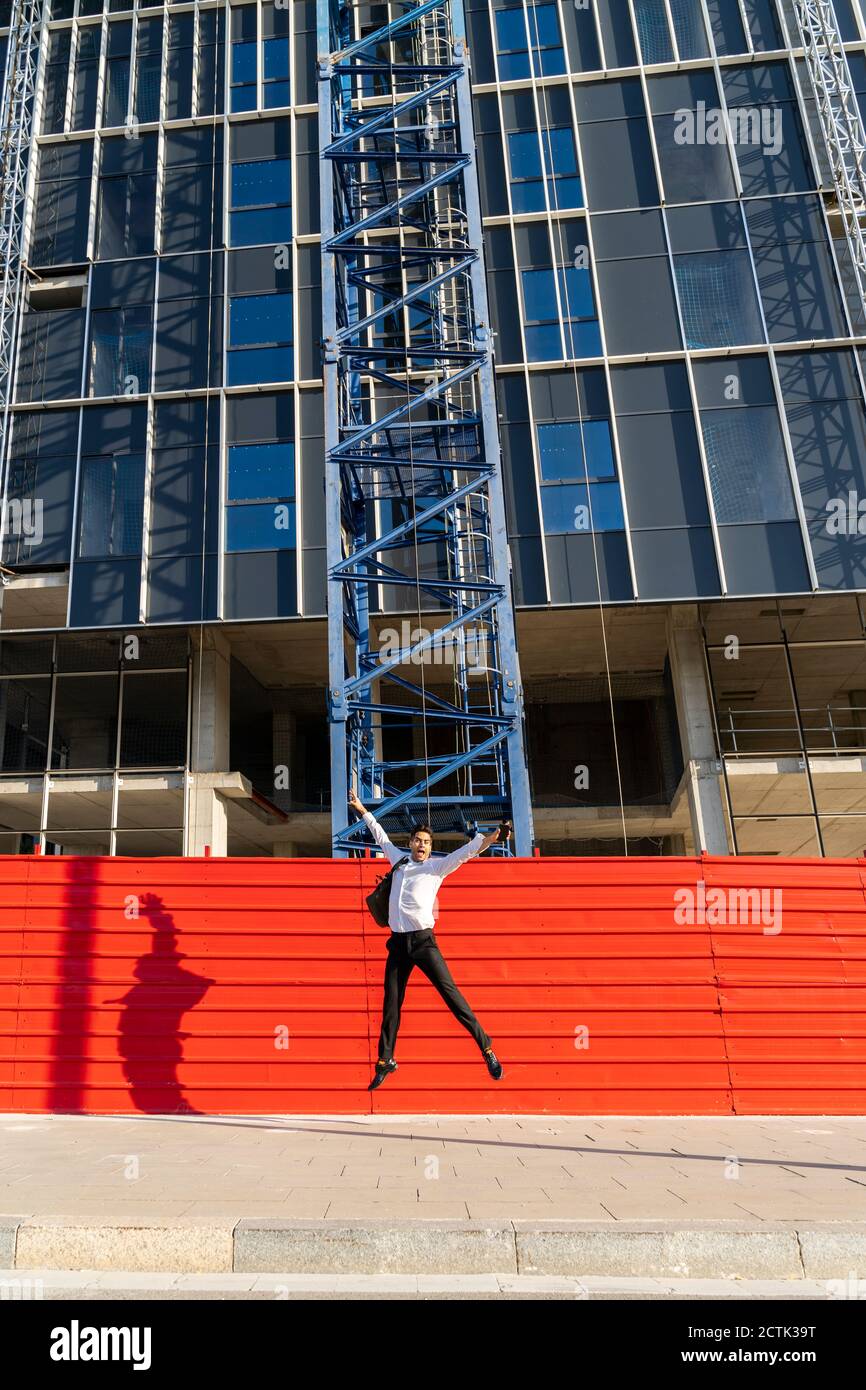 Uomo d'affari allegro con le braccia alzate saltando sul sentiero contro costruito struttura Foto Stock