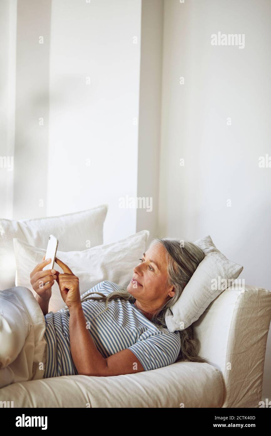 Donna che usa il telefono sul divano in soggiorno Foto Stock