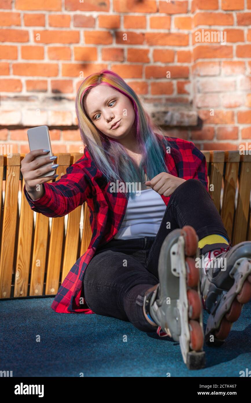 Giovane donna con capelli tinti e pattini a rotelle che prendono un selfie con il suo smartphone, incrociati Foto Stock