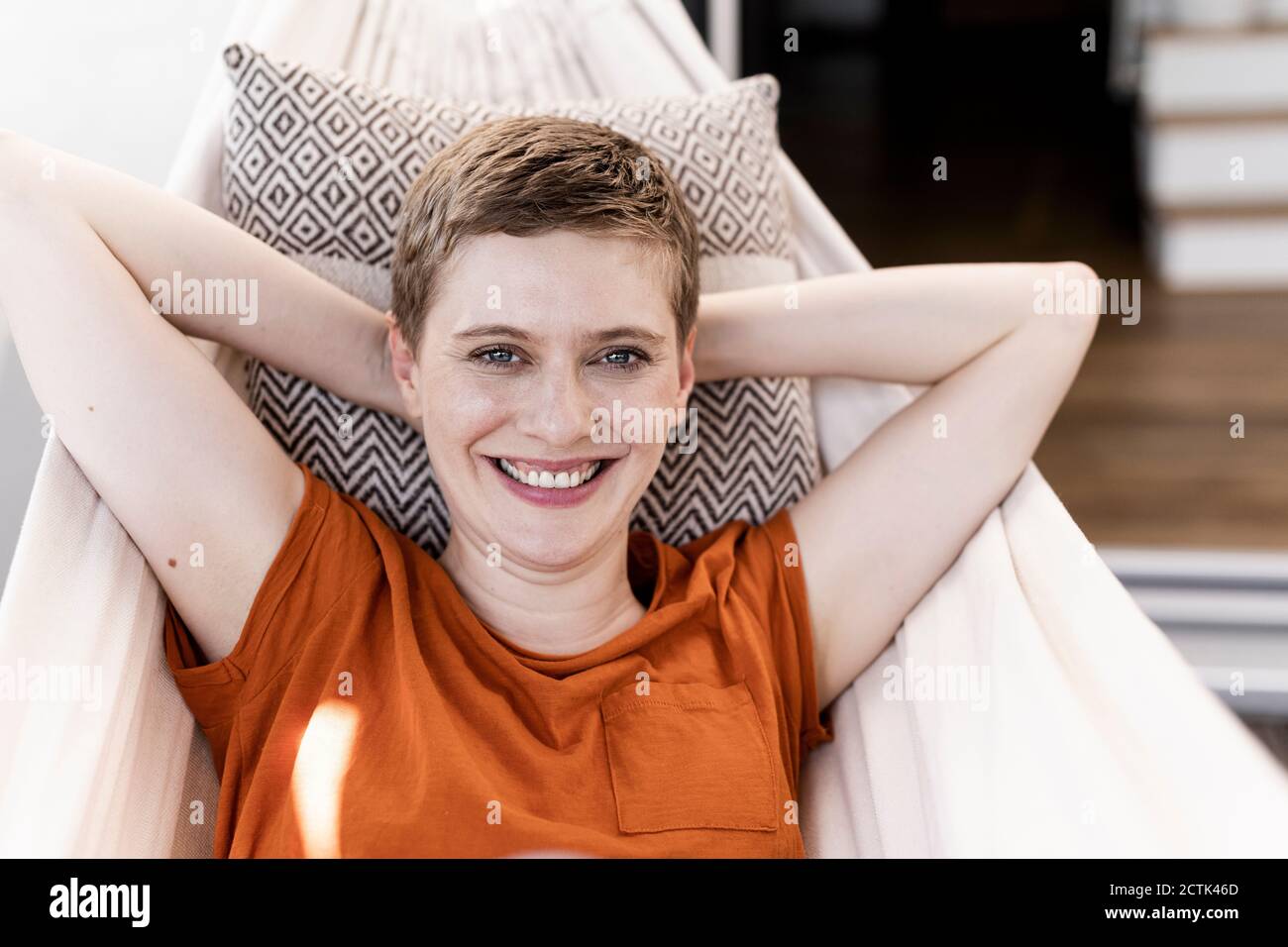 Primo piano di felice bella donna con le mani dietro la testa che riposano su amaca in cortile Foto Stock