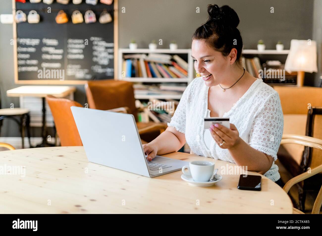 Felice giovane donna che fa lo shopping in linea sopra il laptop nel caffè negozio Foto Stock