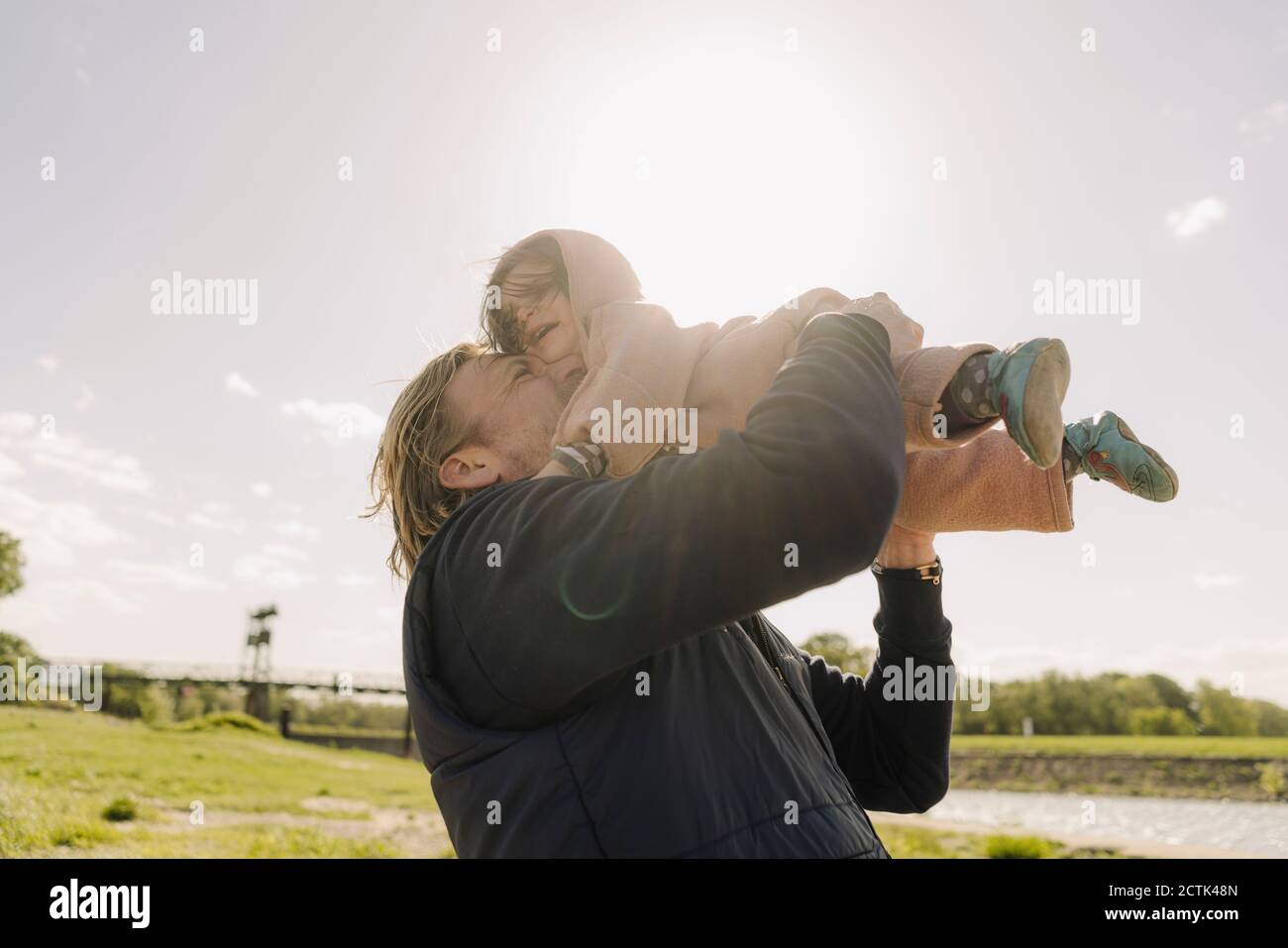 Allegro padre nuzzling figlia mentre la solleva in aria su giorno di sole Foto Stock