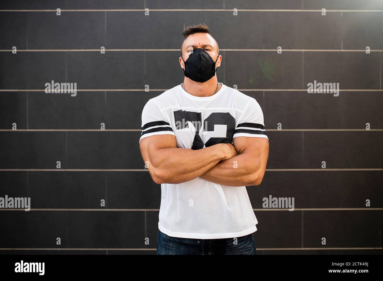 Macho giovane uomo che indossa maschera viso in piedi contro il muro Foto Stock