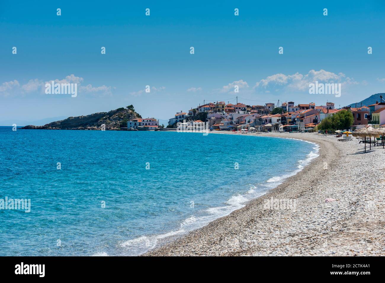 Grecia, Nord Egeo, Kokkari, Rocky spiaggia costiera in estate con villaggio in background Foto Stock