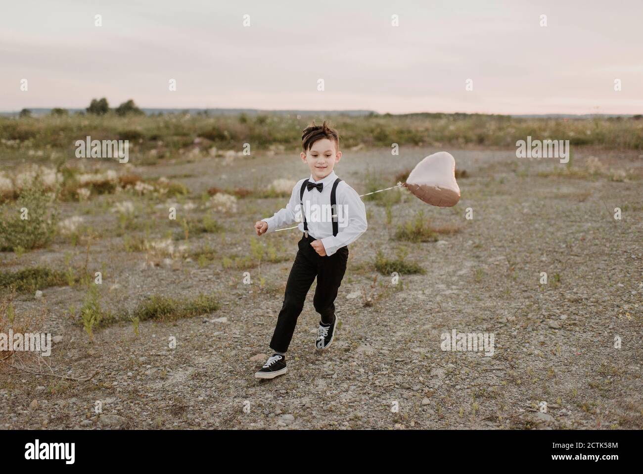 Ragazzo con palloncino a forma di cuore che corre sul campo contro il cielo Foto Stock