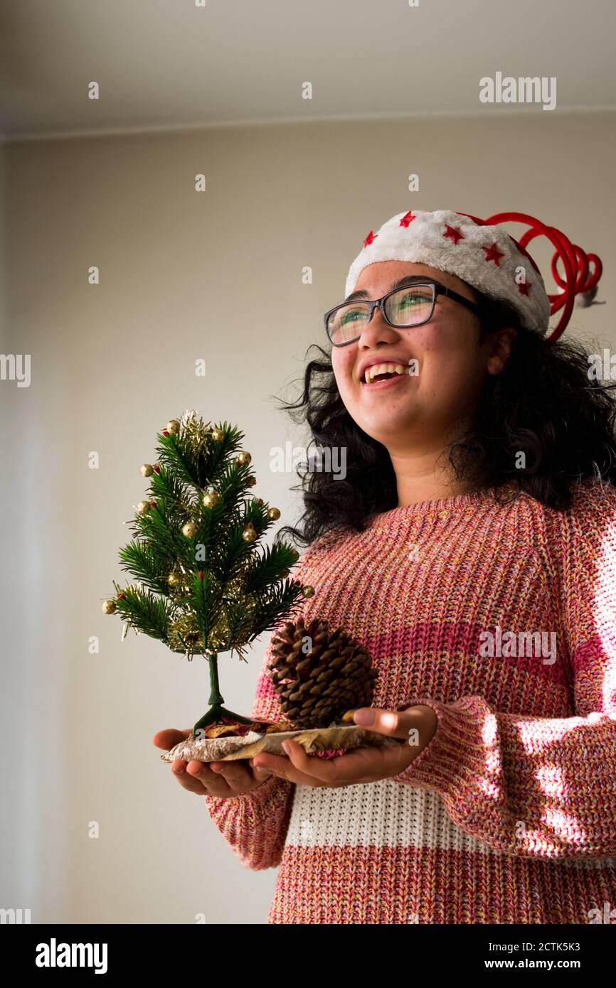 Ragazza latina curly che indossa un cappello rosso di natale e natale maglione a casa con un piccolo albero di natale Foto Stock