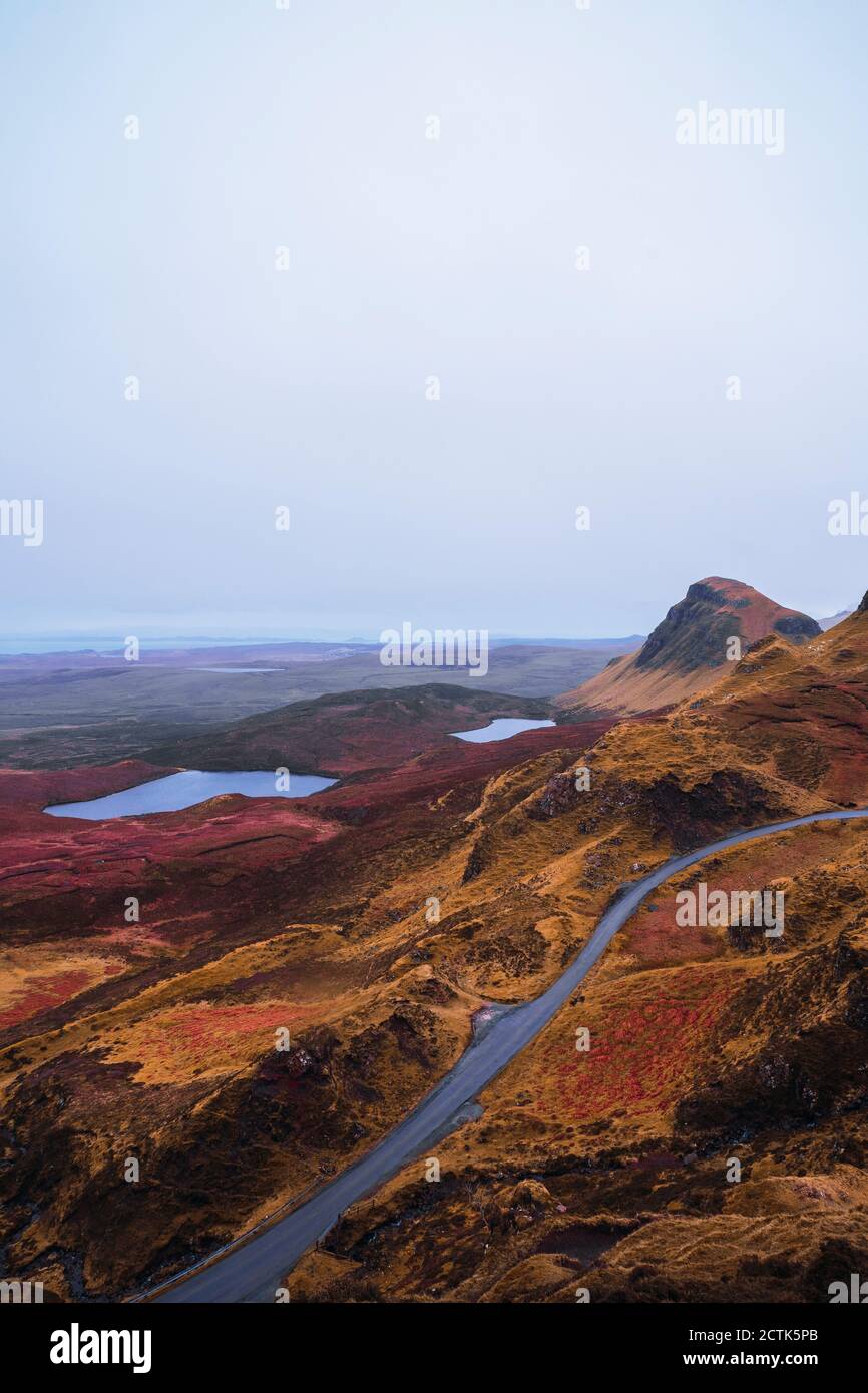 Regno Unito, Scozia, drone vista di autostrada vuota che si estende lungo il paesaggio montuoso marrone dell'Isola di Skye con piccoli laghi sullo sfondo Foto Stock