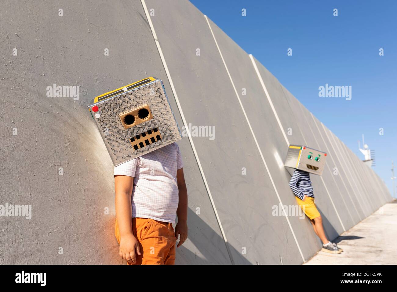 Ragazzi che indossano maschere robot in piedi contro il muro in città giorno di sole Foto Stock