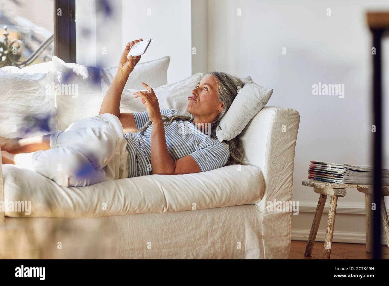 Donna che utilizza il cellulare mentre sdraiato sul divano nel soggiorno Foto Stock