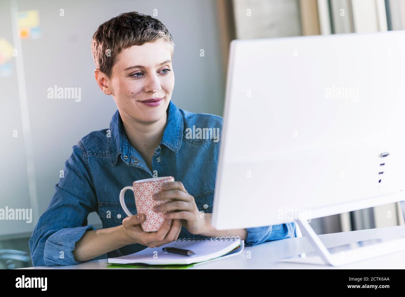 Donna d'affari sorridente alla scrivania in ufficio che guarda lo schermo del computer Foto Stock