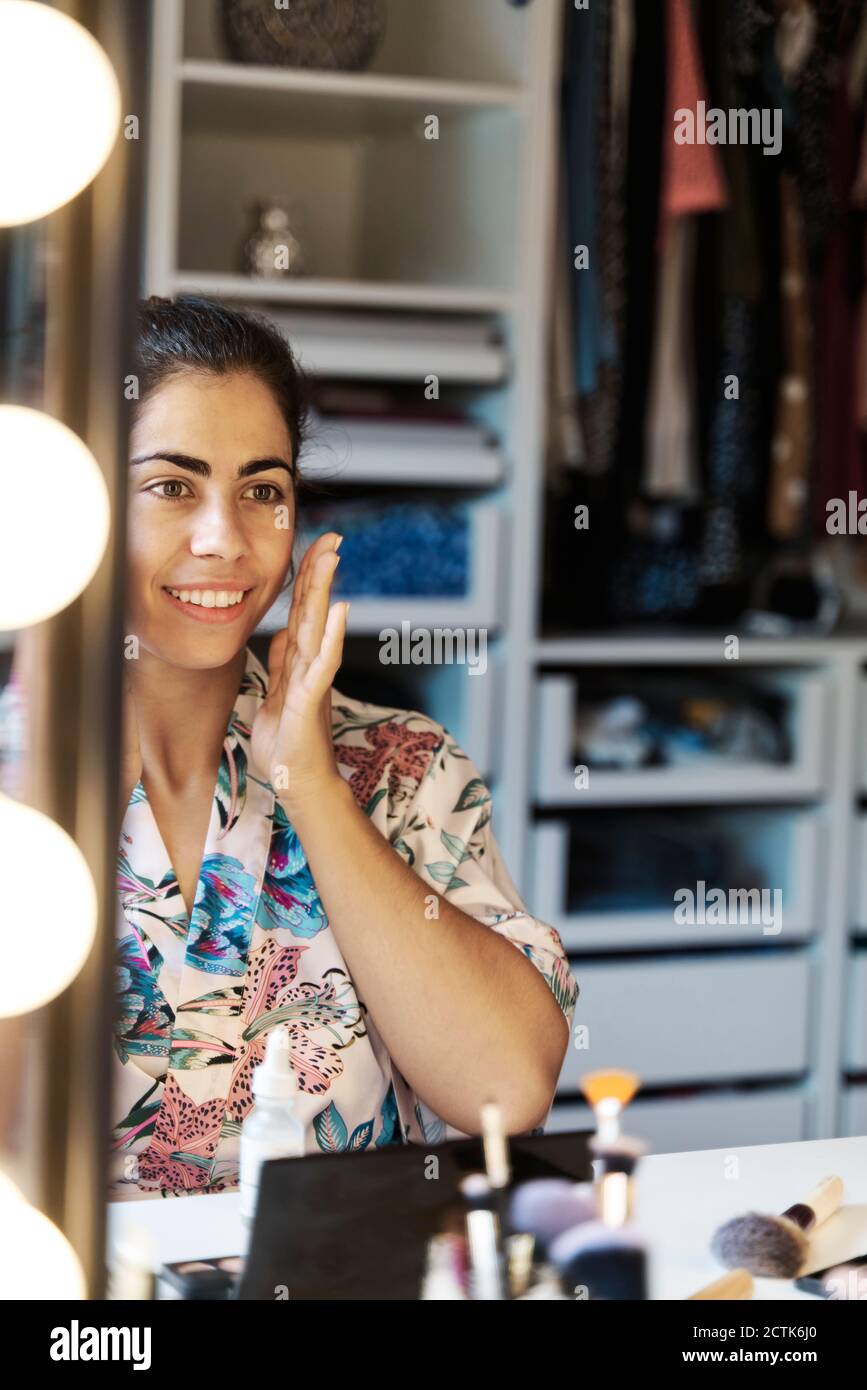 Riflessione della giovane donna sullo specchio mentre si passa attraverso la mattina routine di bellezza a casa Foto Stock