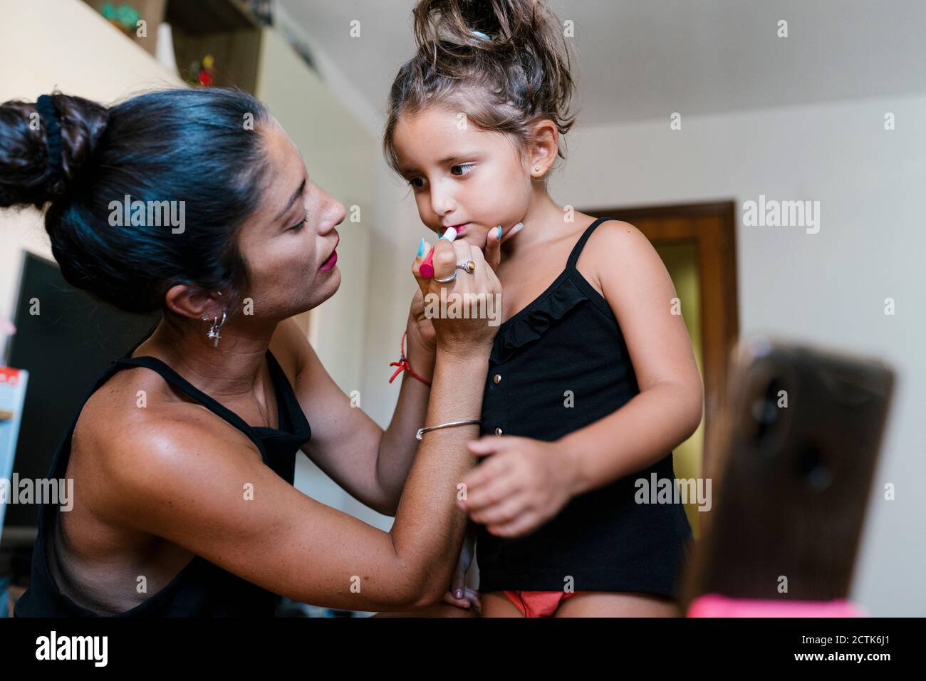 Madre che mette il rossetto alla figlia durante la registrazione video a casa Foto Stock
