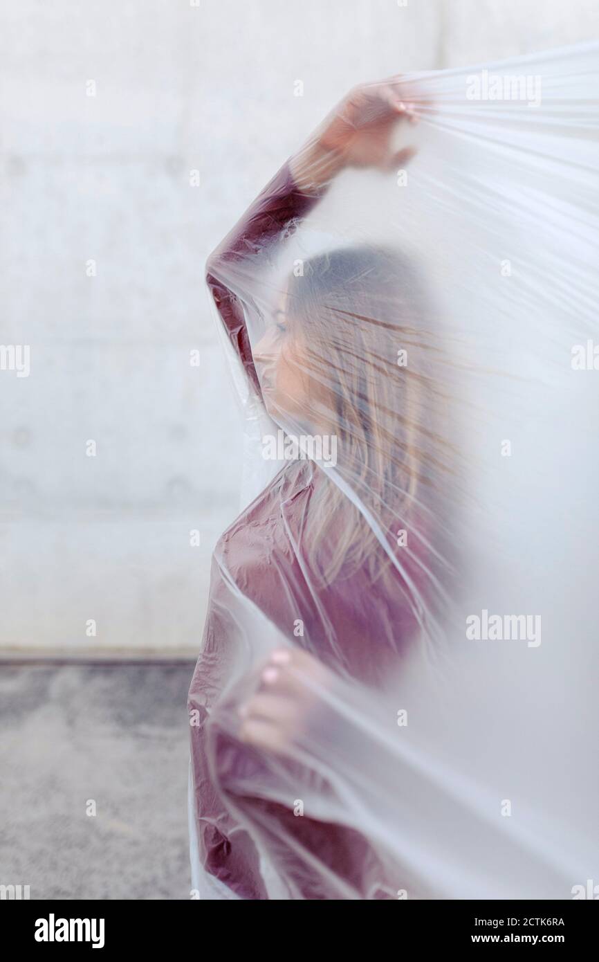 Donna che fa i gesti della mano mentre si copre in plastica contro muro di cemento Foto Stock