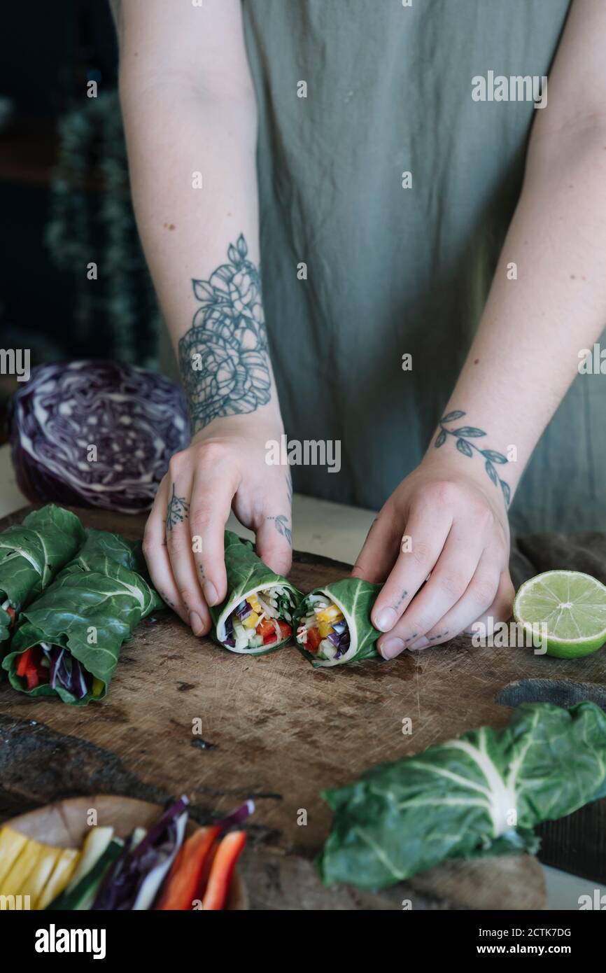 Giovane donna che prepara il rotolo vegano con le verdure sul tagliere Foto Stock