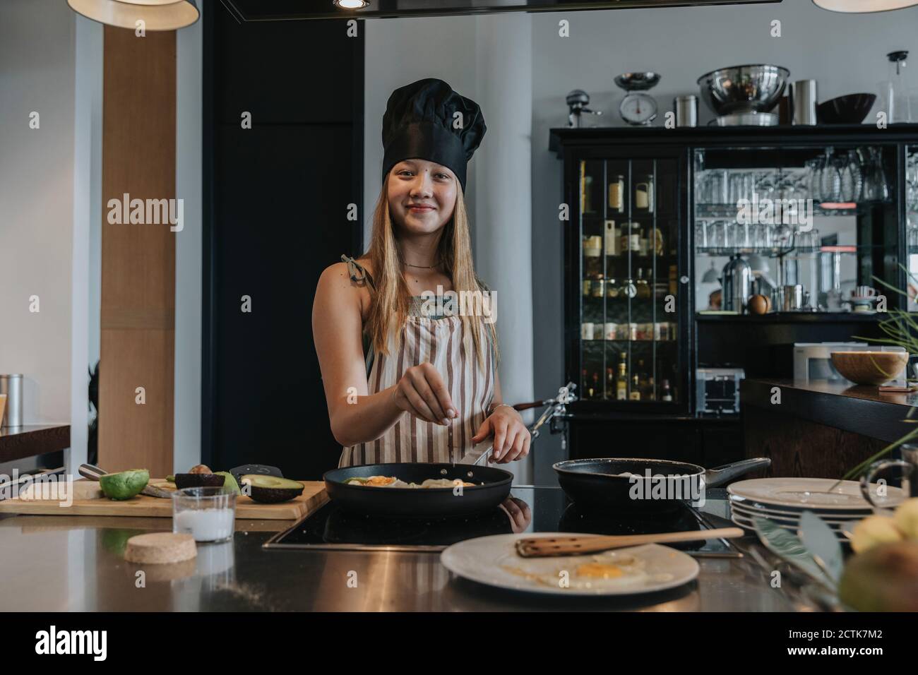 Ragazza adolescente che prepara un pranzo sano in cucina, indossando il cappello dello chef Foto Stock