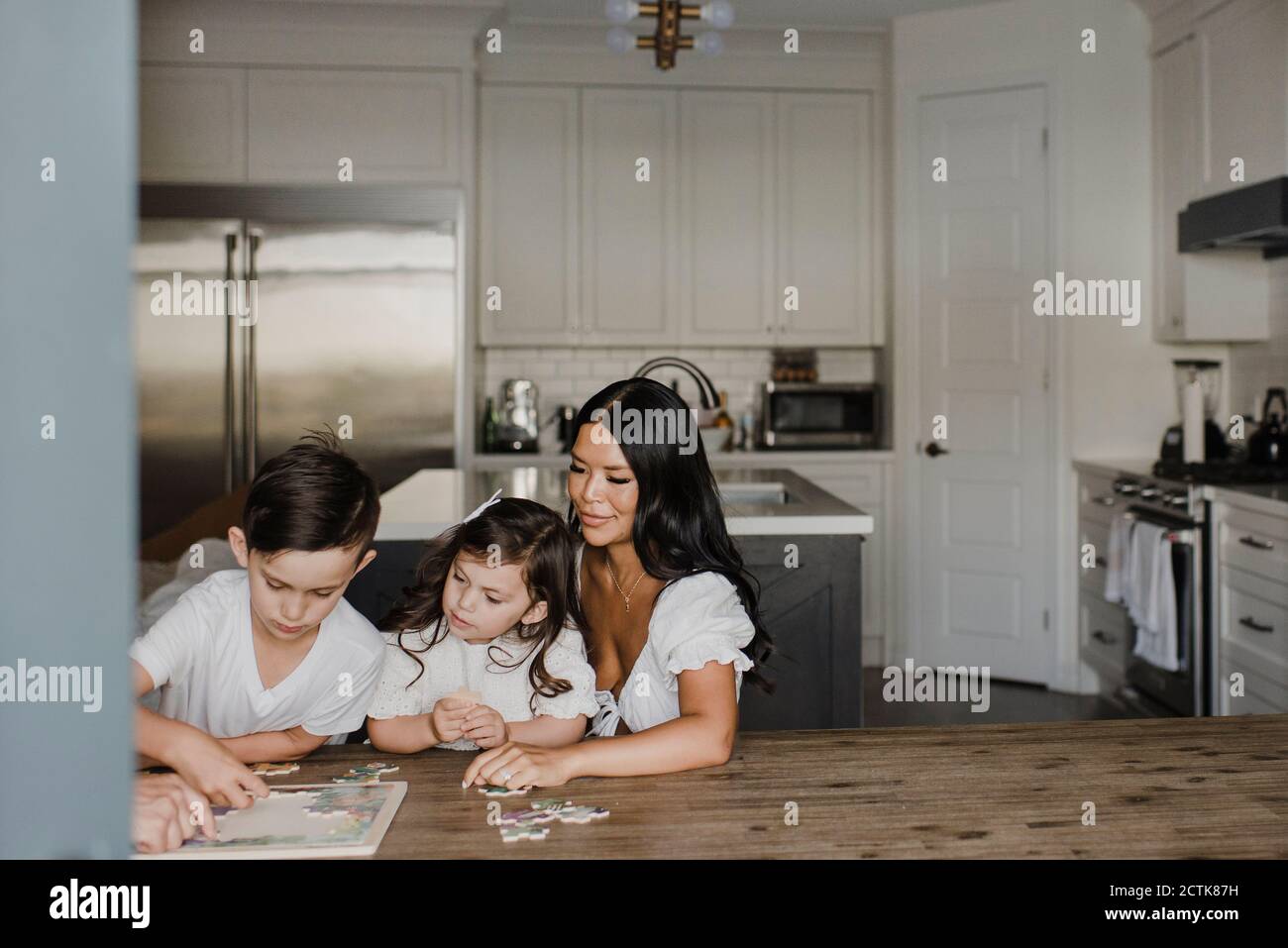 Sorridente genitori risolvere il puzzle con i bambini sopra il tavolo a casa Foto Stock
