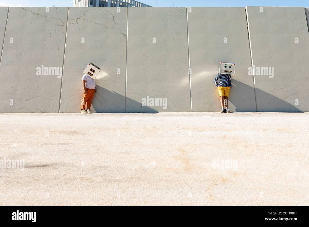 Amici che indossano maschere robot in piedi contro il muro in città giorno di sole Foto Stock