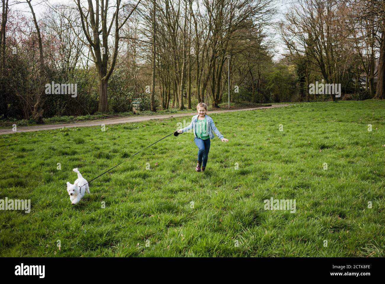 Ragazza sorridente che corre con il cane su erba in cortile Foto Stock