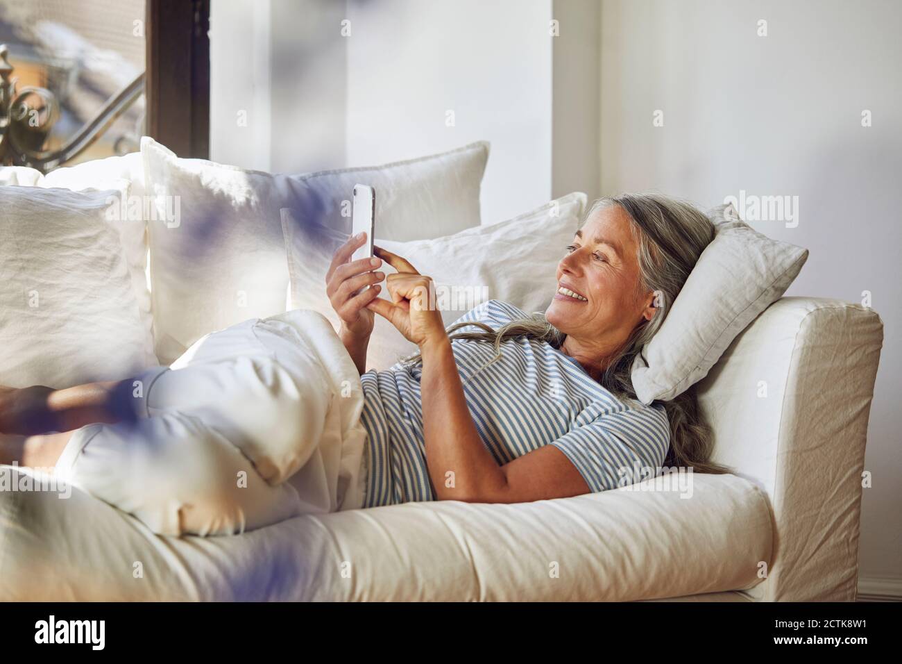Donna sorridente che usa il telefono sul divano in soggiorno Foto Stock