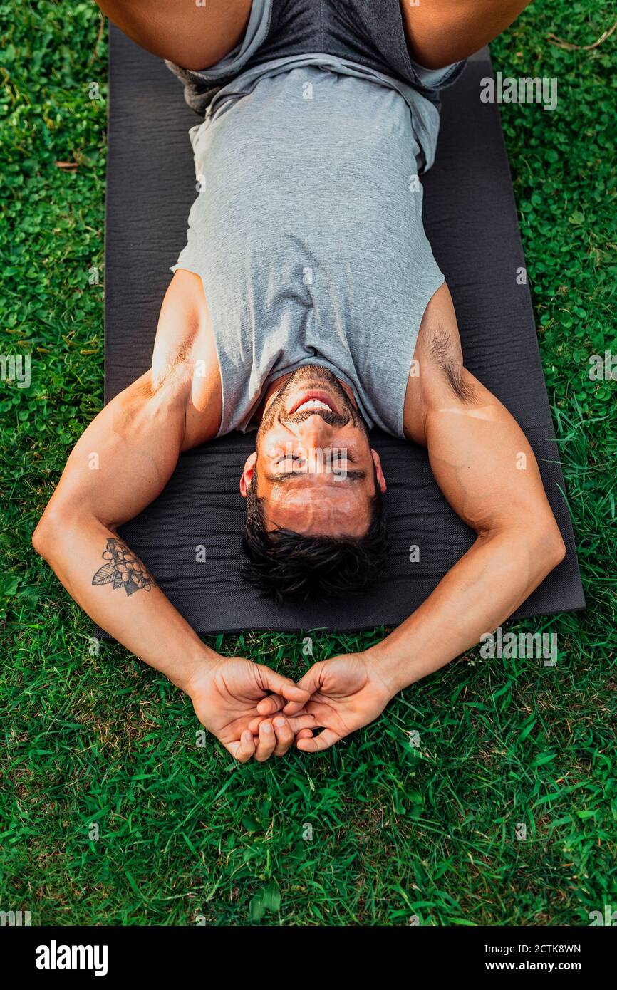 Uomo sorridente sdraiato sul tappeto da ginnastica nel parco Foto Stock