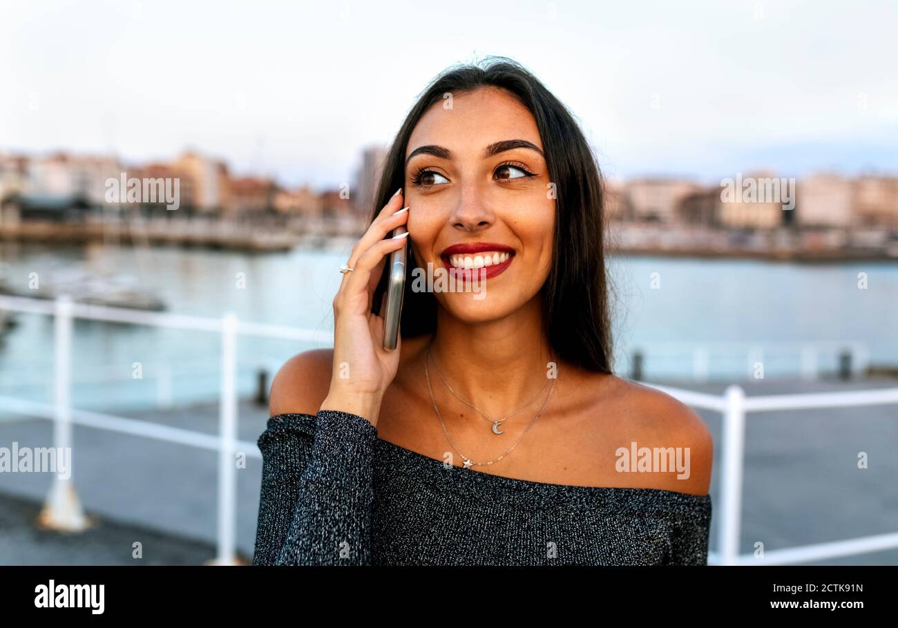 Giovane donna che parla al telefono mentre si è in piedi sul lungomare Foto Stock