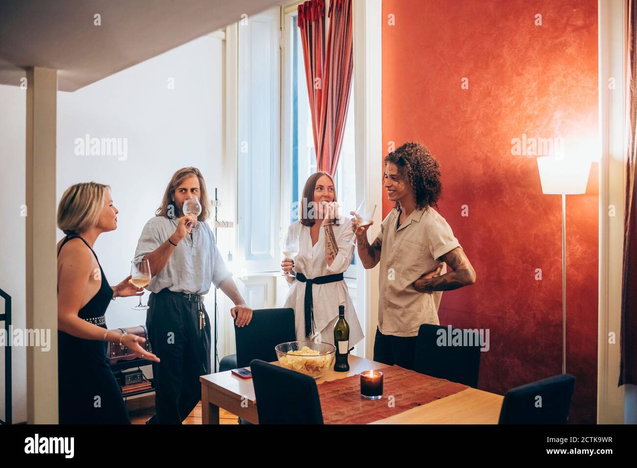 Amici di sesso maschile e femminile godendo del vino durante la riunione sociale a. casa Foto Stock